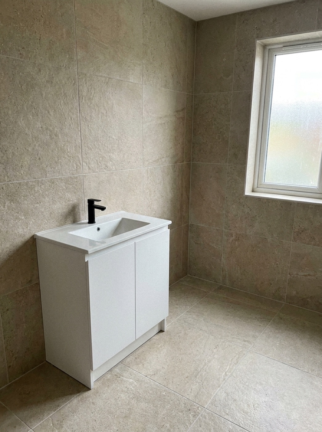 Sunlit ensuite with beige stone-look wall and floor tiling and white vanity